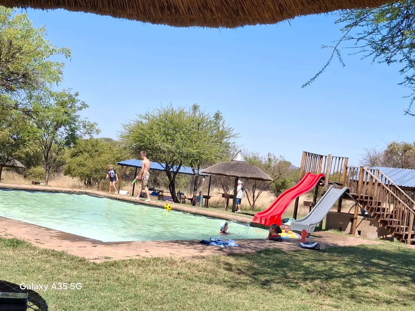 Kids' pool with red and grey slides, thatch shade and camp seating