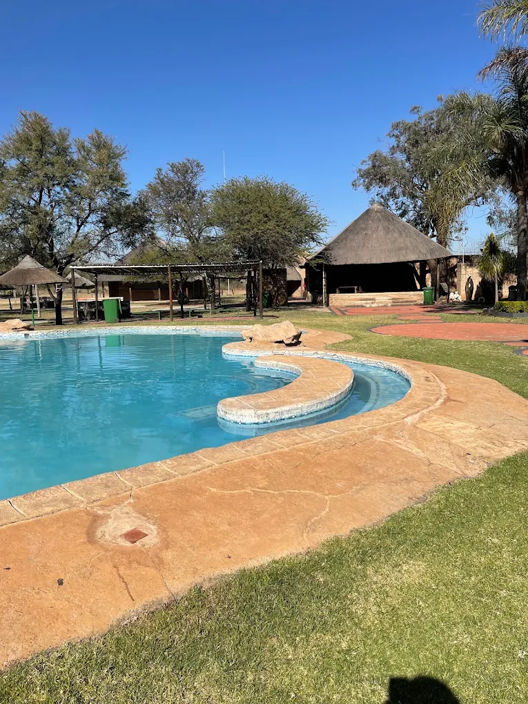 Pool with a curved shallow shelf, lawn and a thatch lapa under a clear sky