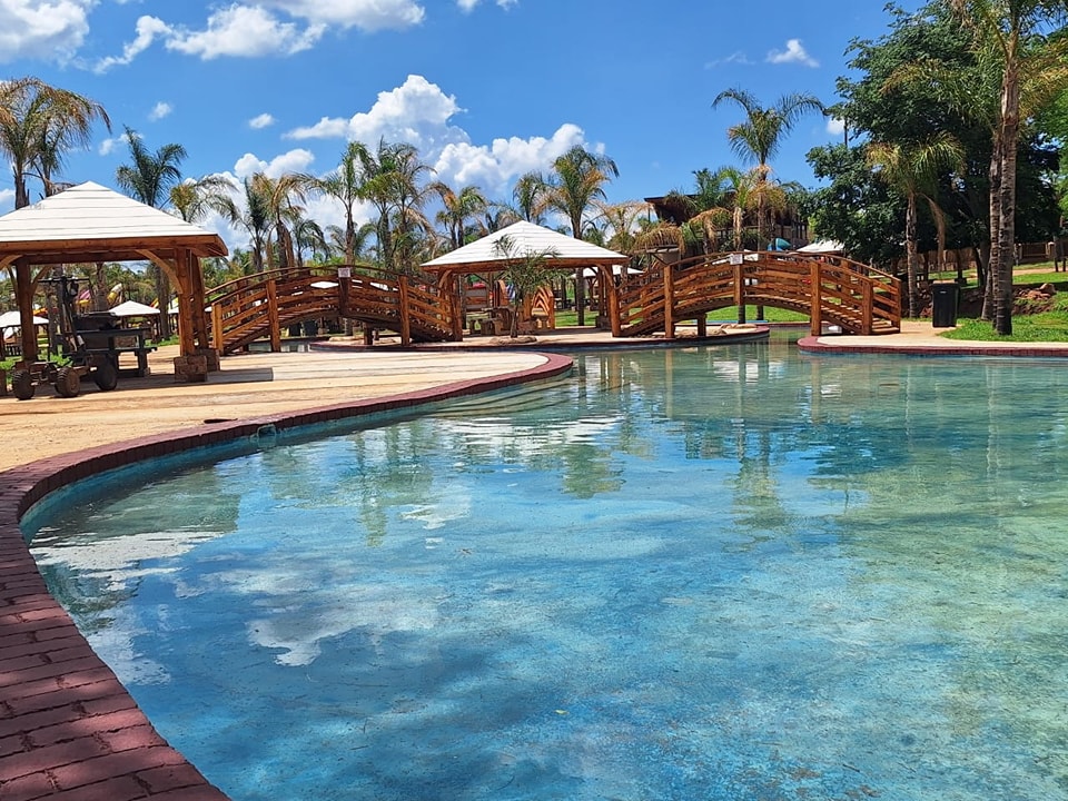 Curved pool with wooden bridges, white shade gazebos and a braai stand