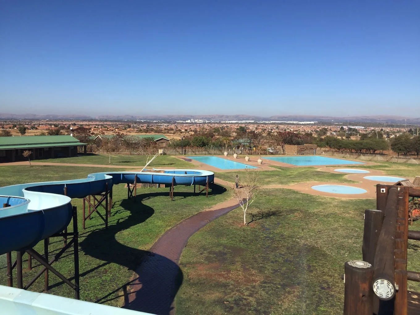 Wide view of the winding blue slide, three pools and Soshanguve beyond
